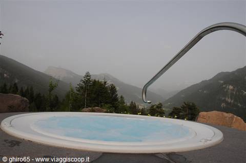 Whirlpool tub with turquoise water amid mountains and firs, hazy sky