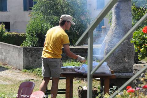 Young man in cap and yellow shirt grilling food in the garden