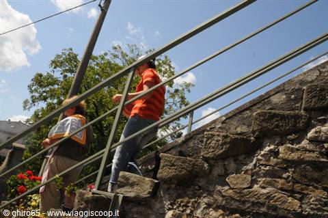 Tourist in orange shirt climbs stone steps with green metal handrail under blue sky
