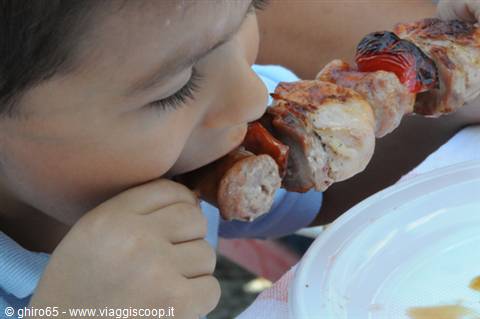 Child biting a grilled meat and pepper skewer