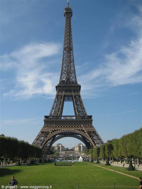 The iron Eiffel Tower rises above the green Champ de Mars, blue sky