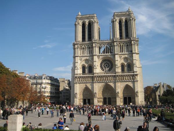 Crowds of tourists fill the square before Notre-Dame's Gothic facade under blue sky