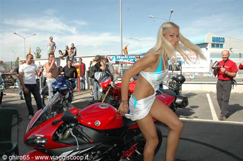 Blonde girl in light blue bikini posing beside a red Yamaha among the crowd
