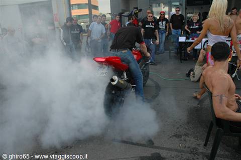 Motorcyclist performs a burnout in white smoke, crowd gathered in an urban yard