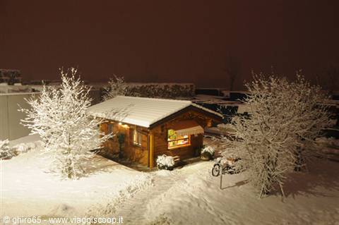 Wooden chalet lit at night in snow, frosted trees and a parked motorcycle