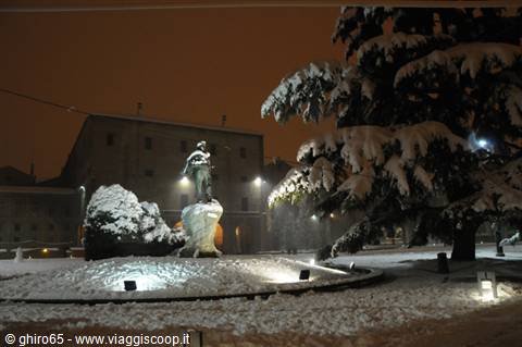 Snow-covered equestrian statue at night, orange light on cedar trees