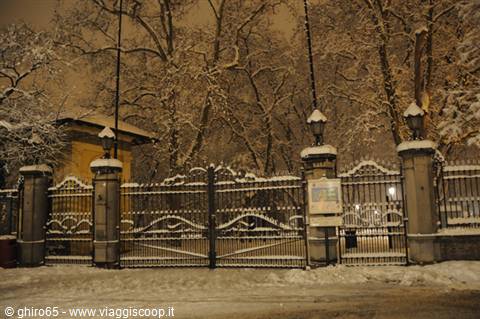 Snow-covered wrought iron gate at night between stone pillars and lampposts