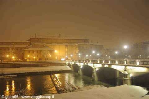 Illuminated bridge over snowy river at night, lights reflecting on water