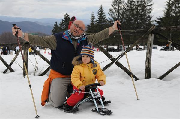 Man and child with sled on snow, ski poles, wooden fence and mountains