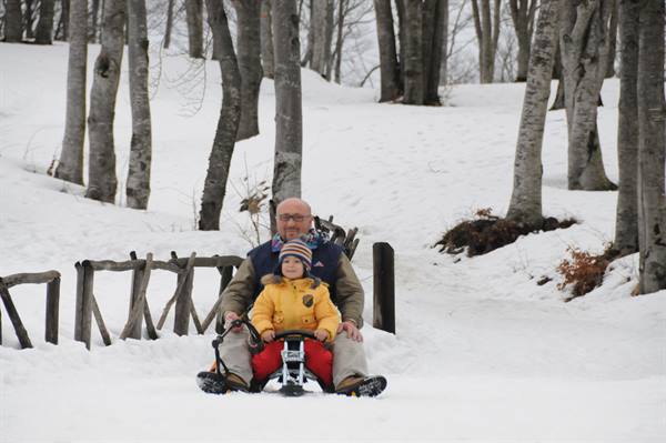 Child in yellow snowsuit and grandpa on a sled in snowy woods