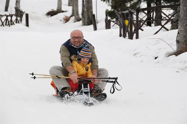 Dad and child sledding down a snowy path between wooden fences