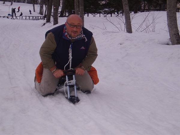 Man with glasses on a snow sled among bare trees