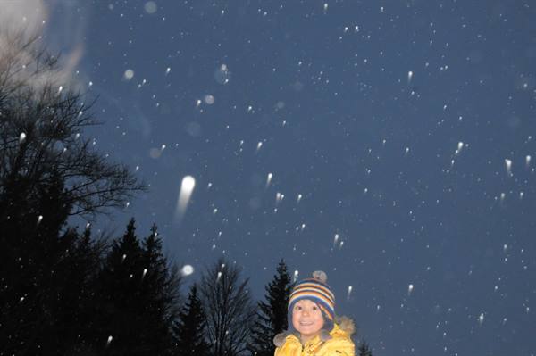 Child in striped hat and yellow jacket under falling snow at night