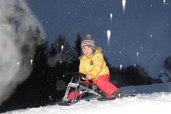 Child in yellow jacket and striped hat rides a sled down the snow