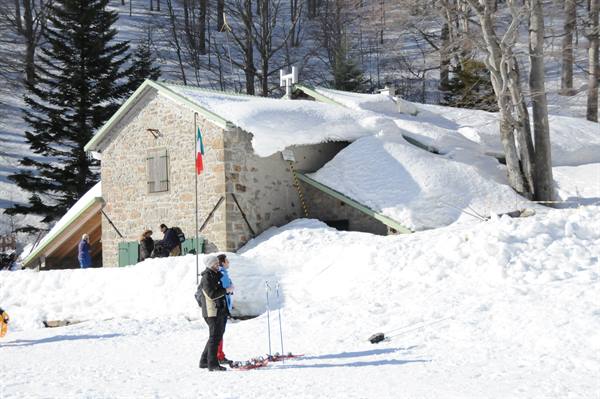 Skiers with snowshoes near a snow-covered stone mountain hut