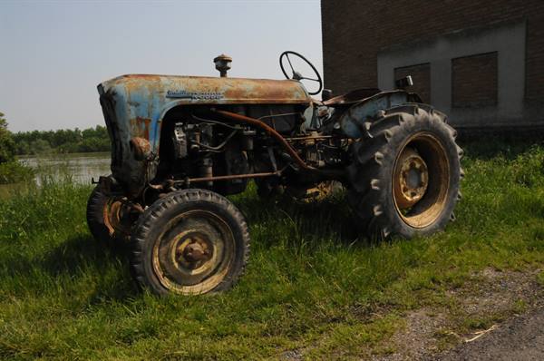 Rusty old Lamborghini tractor abandoned in the grass beside a barn