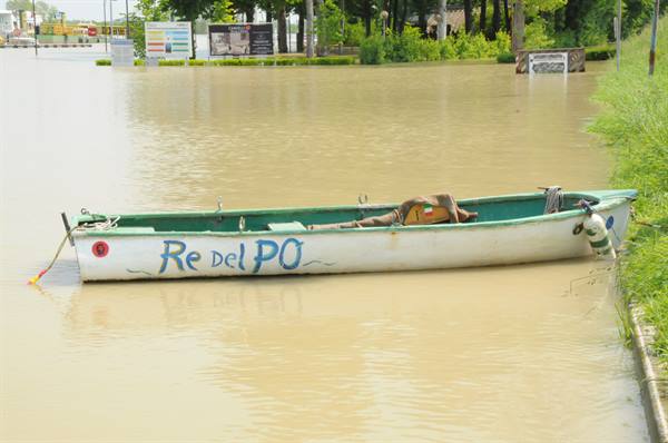 White boat Re del Po moored on muddy floodwater beside grassy embankment