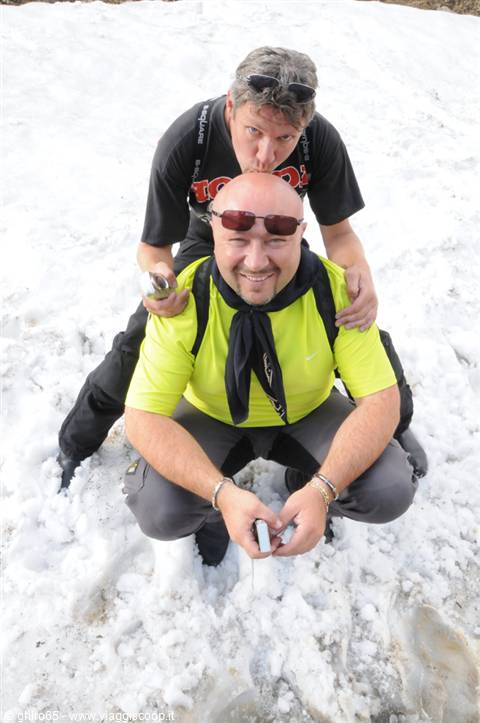 Two men joking on the snow, one in yellow shirt hugging his friend