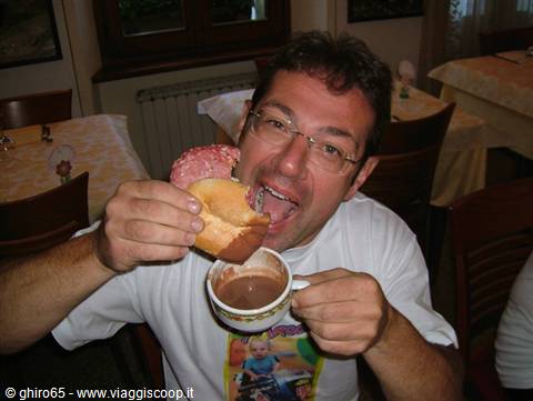 Man with glasses in a trattoria, dipping bread with mortadella into hot chocolate