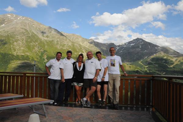 Group of friends in white polo shirts on wooden terrace among green mountains and cloudy sky