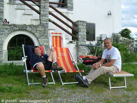 Two men sitting on orange deck chairs outside a stone house