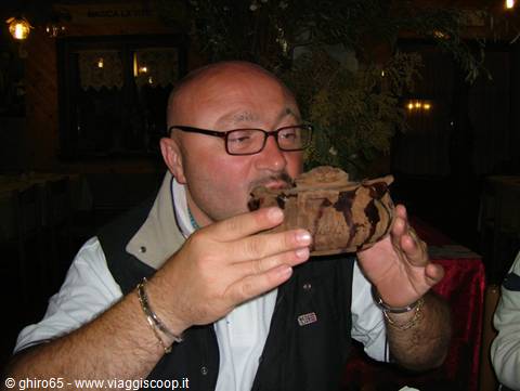 Man with glasses drinking from a traditional wooden and leather flask indoors