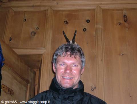 Smiling man wearing goat horns on his head inside a wooden hut