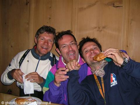 Three friends laughing and eating snacks inside a wooden hut