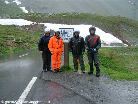 Four motorcyclists in rain suits beside the Albula pass sign at 2315m, snow