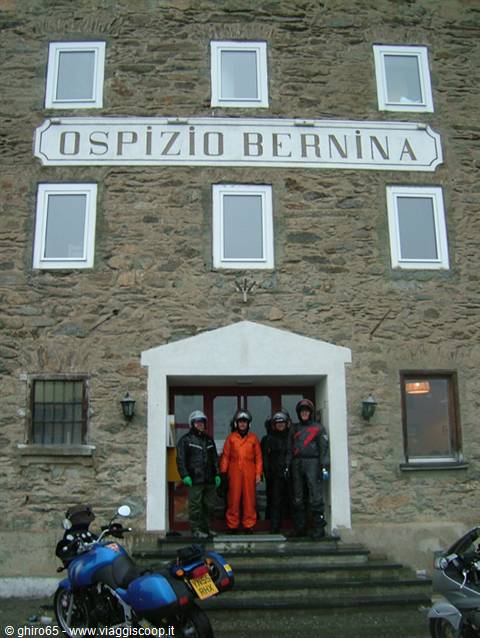 Four motorcyclists in rain suits at the Ospizio Bernina entrance, stone building
