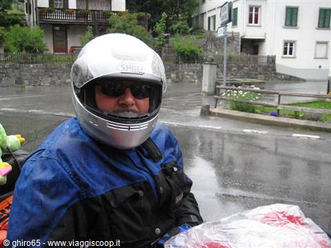 Motorcyclist in silver helmet and blue jacket on wet road among houses