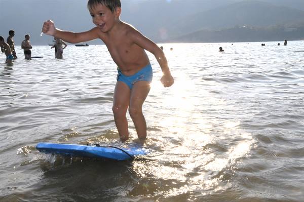 Boy in blue swimsuit balancing on a bodyboard in the shallow waves