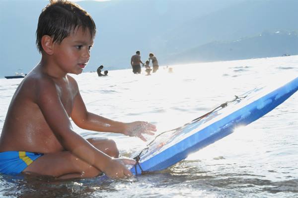 Wet boy in water with blue bodyboard, people in sunny background