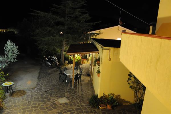 Stone courtyard with table and parked scooter, warm house lights at night