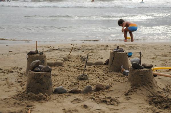 Sandcastle with stones and sticks, child playing near the waves