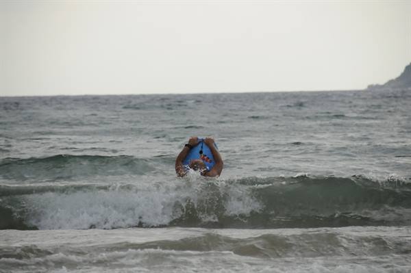 Child on blue bodyboard in ocean waves, overcast sky