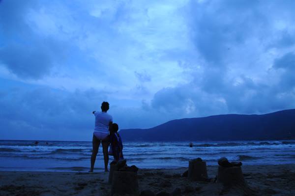 Woman and child on beach with sandcastles, cloudy sky