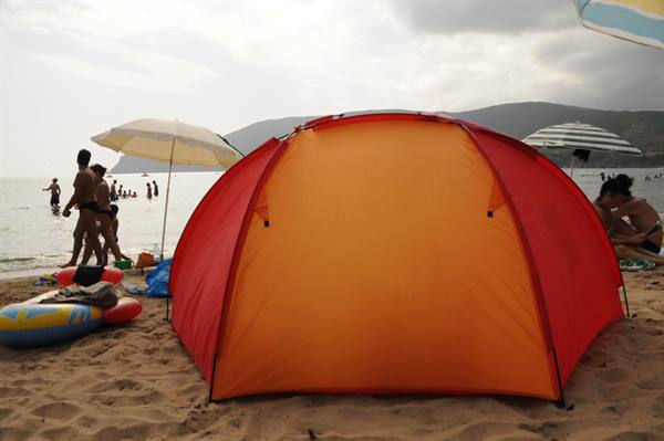Orange and red tent on the sand, swimmers and umbrellas by the sea