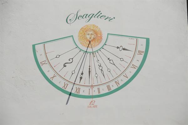 Painted sundial on white wall with golden sun and Scaglieri inscription