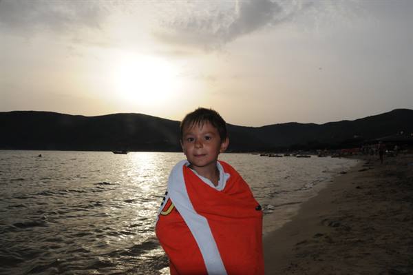Child wrapped in red towel on the beach as light fades