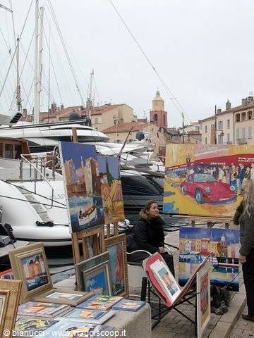 Painter displays harbor paintings at Saint-Tropez port among sailing yachts