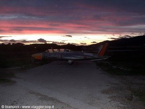 Old silver and orange military jet parked on a dirt strip among hills