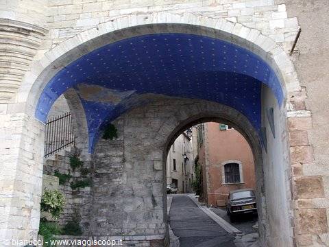 Stone gateway with blue star-painted vault over narrow lane with parked car