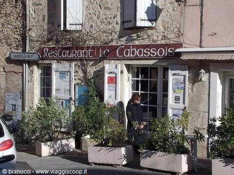 Woman outside Le Cabassois restaurant, red sign on stone facade