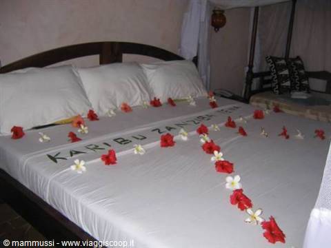 Bed decorated with red and white flowers spelling Karibu Zanzibar, canopy room