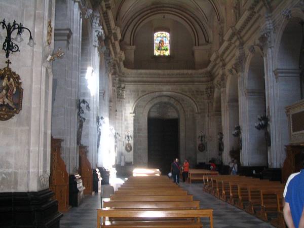 Inside a baroque stone church with wooden pews and visitors