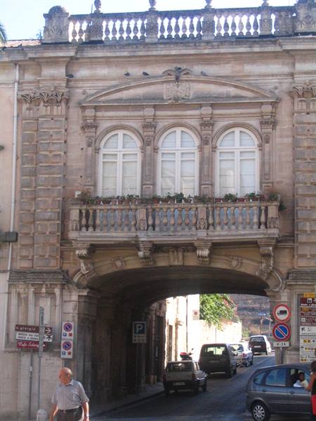 Baroque stone palace with balcony above the arch, cars passing underneath