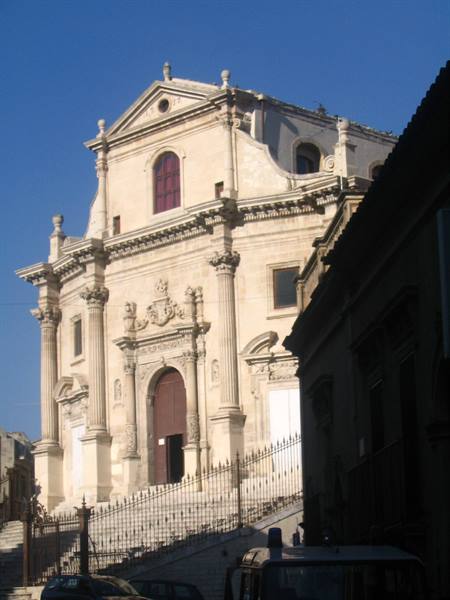 Baroque stone church with staircase and iron fence under blue sky
