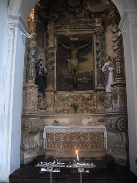 Carved stone altar with painted crucifix, side statues and a lit candle