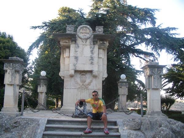 Man sitting on steps of the stone Pro Patria monument, among chains and conifers